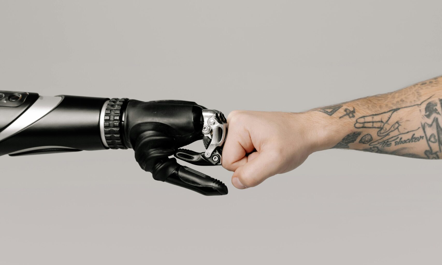 A human fist bumping with a prosthetic arm on a neutral background.